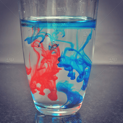 Blue and red dye naturally mixing in a cup of water.